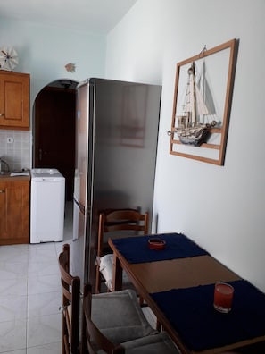 Una cocina pequeña con un refrigerador, una mesa de madera con un mantel individual azul y una silla.