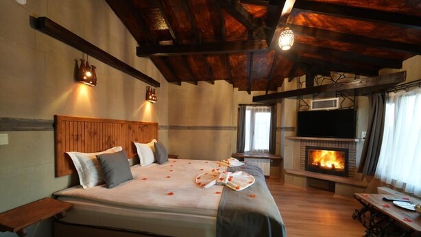 A cozy room with a bed, a fireplace, a TV, and a wooden ceiling. - Kapadokya Konak (Nevsehir)