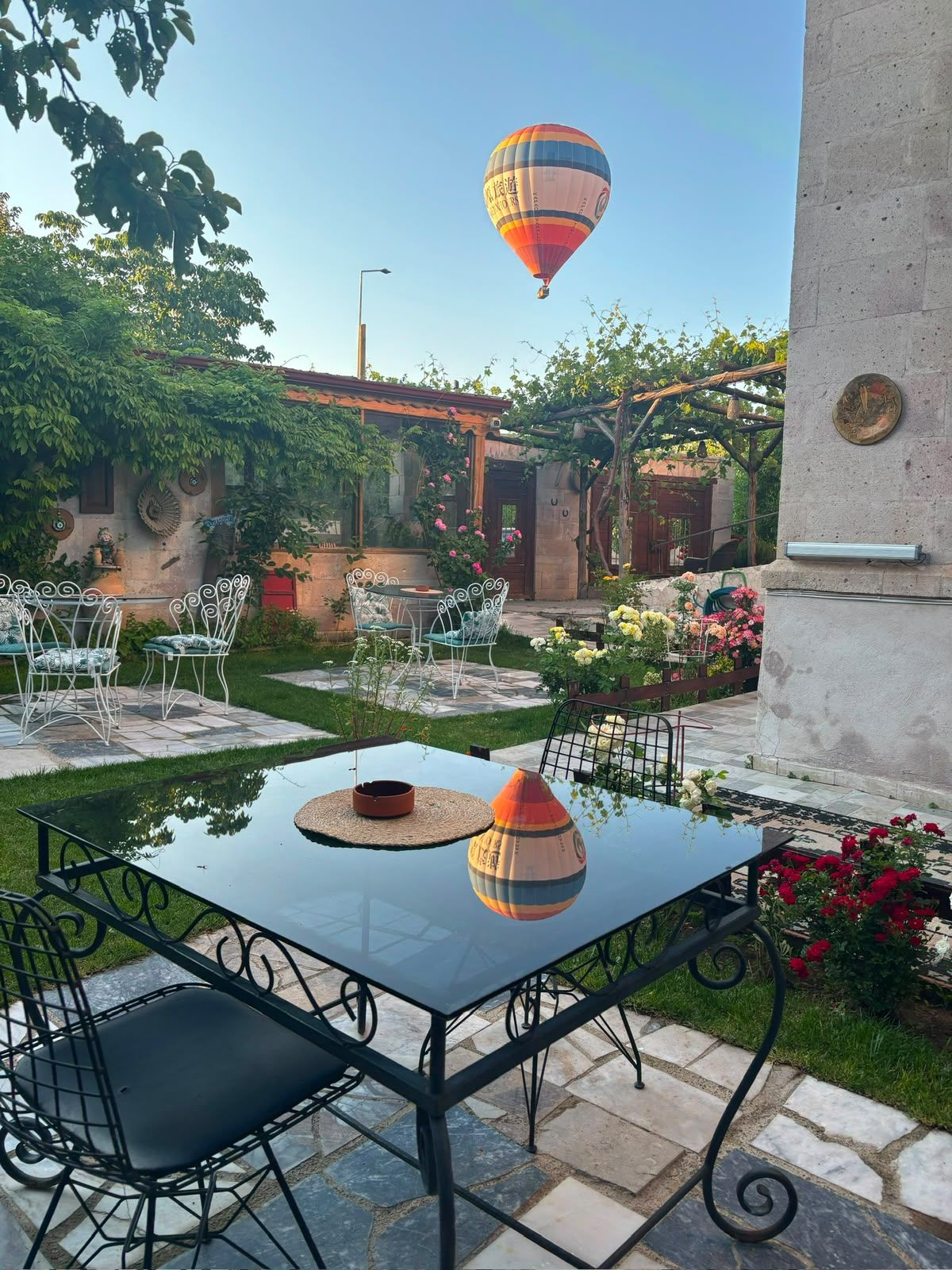 An outdoor patio with a glass table, metal chairs, and a hot air balloon in the background.