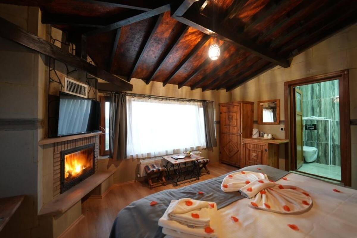 A cozy room with a fireplace, a bed with towels, a wooden desk, and a bathroom with a glass shower.
