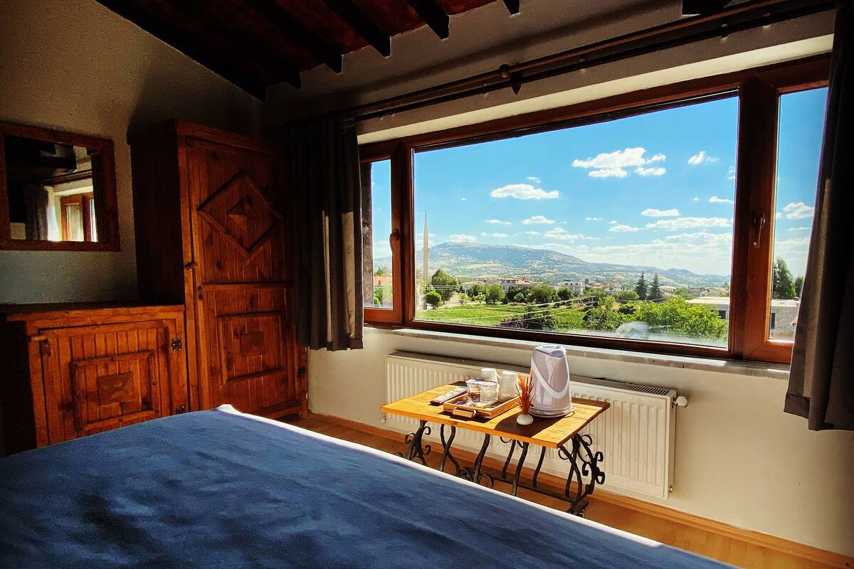 A bedroom with a large bed, wooden wardrobe, and a window with a view of a landscape.