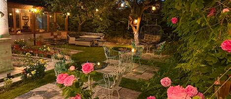 A garden with a seating area, a pond, and a variety of plants and flowers.