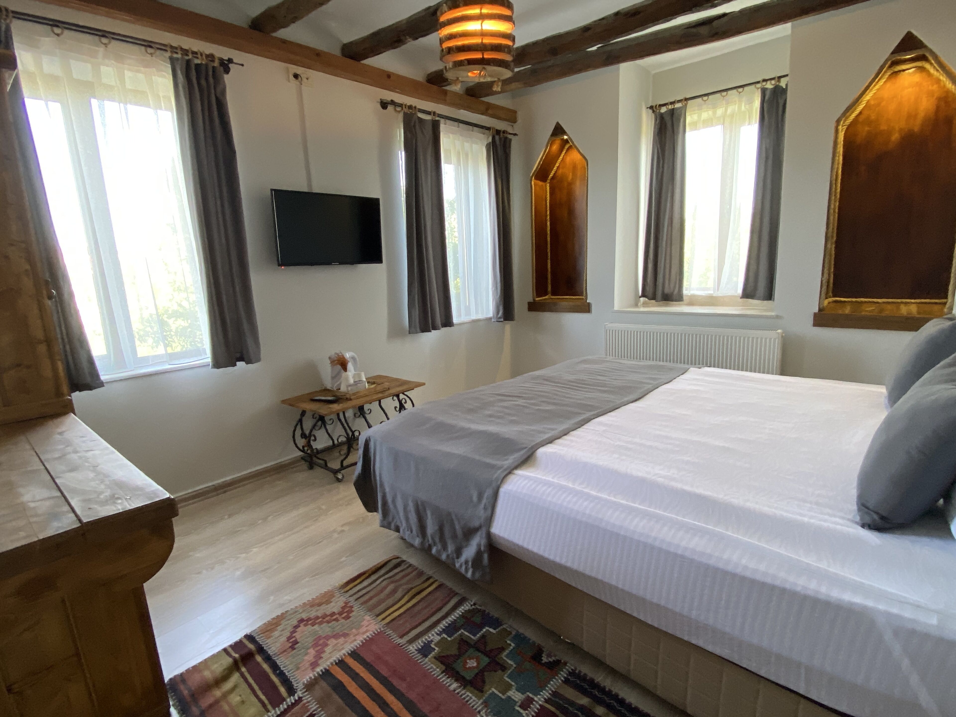 A bedroom with a large bed, a TV, a wooden desk, and a window with curtains.
