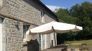 Un bâtiment en pierre avec une table de pique-nique en bois et un parasol blanc.