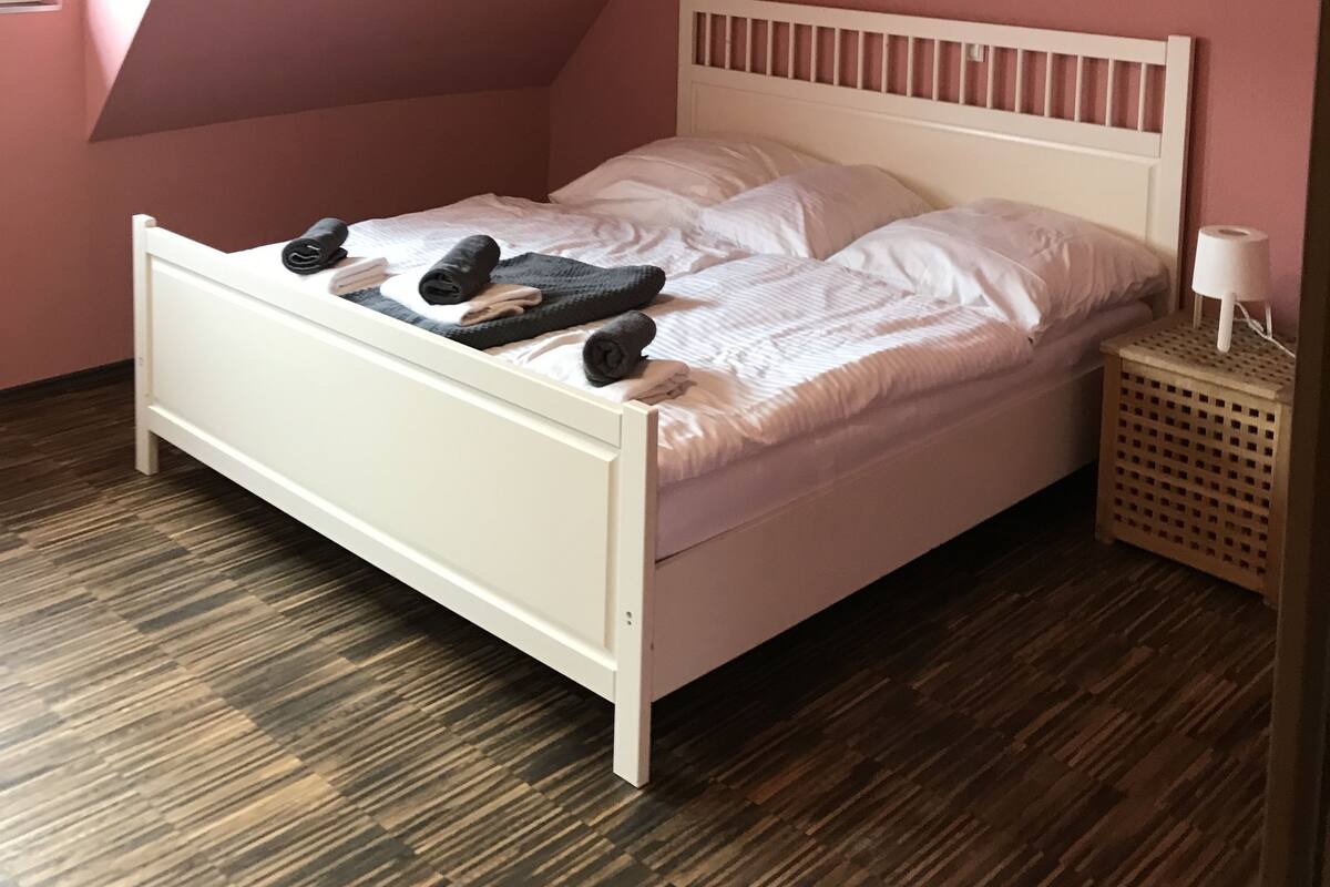A bedroom with a sloped ceiling, a white bed, and a small bedside table with a lamp.