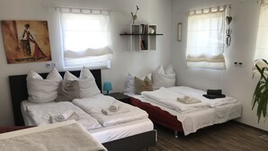 A hotel room with two beds, a desk, a chair, a plant, and a painting on the wall. - Schön Apartments (Ohmden)