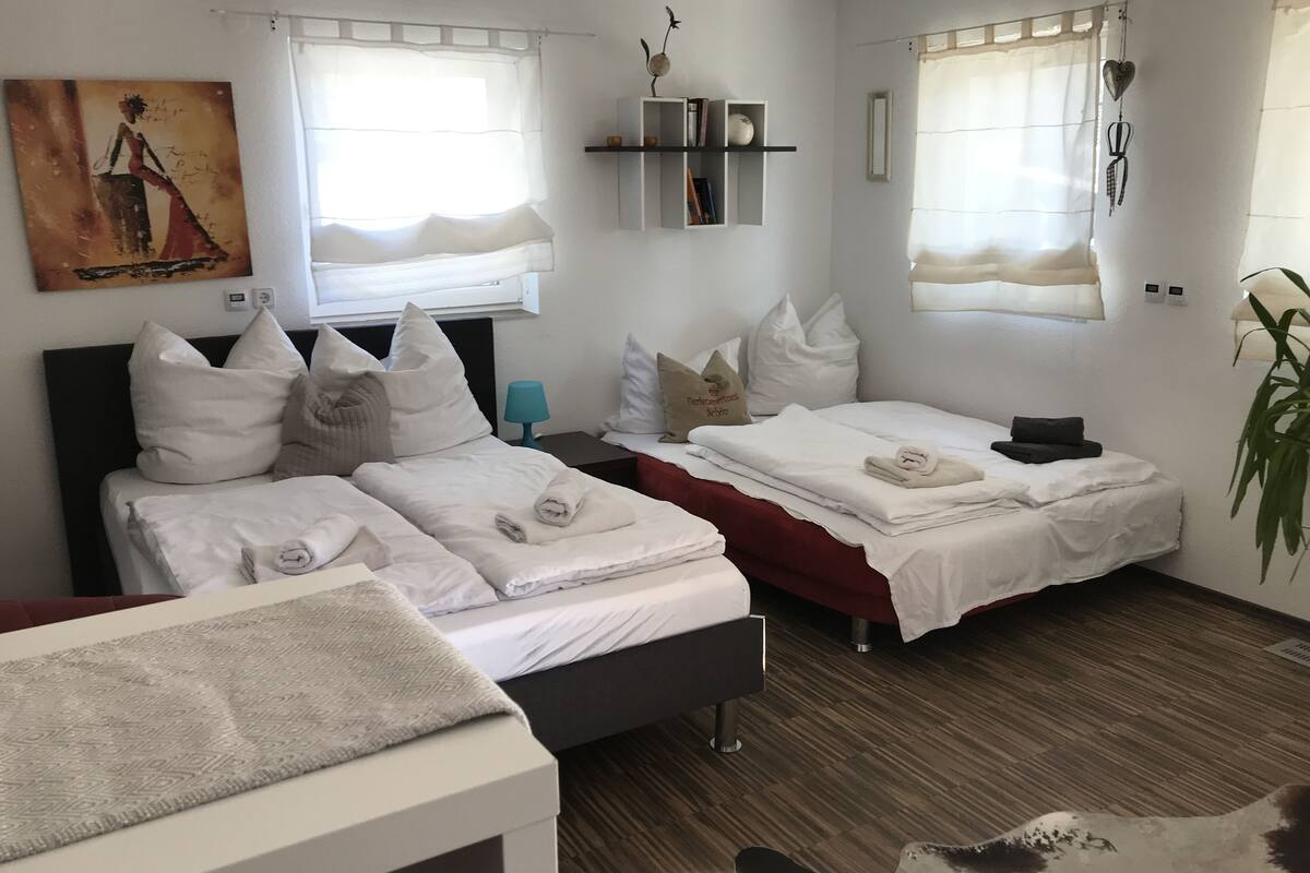 A hotel room with two beds, a desk, a chair, a plant, and a painting on the wall.
