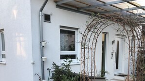 A white building with a metal gate, a small garden, and a paved walkway. - Schön Apartments (Ohmden)