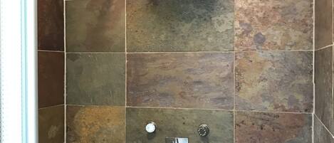 A shower with a handheld showerhead and a wall-mounted control panel with four knobs.
