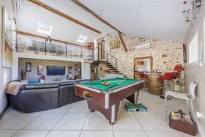Ein großzügiger Wohnbereich mit Billardtisch, einer Couch, einem Fernseher und einer Steinwand.