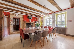 A dining area with a wooden table, wicker chairs, a chandelier, and a kitchen visible through an open door.