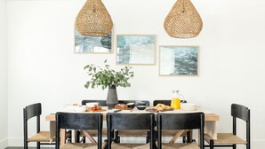 Een eethoek met een houten tafel, zwarte stoelen en geweven hanglampen.