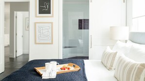Een moderne hotelkamer met een bed, een dienblad met ontbijtartikelen en een schuifdeur naar een badkamer.