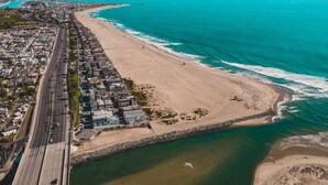 Luchtbeeld van een kuststad met een lang strand, een weg parallel aan de kustlijn en een rotsenrij voor de kust.