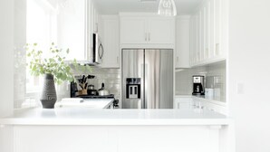 Een moderne keuken met witte kasten, een groot eiland met barkrukken, hanglampen en een koelkast.