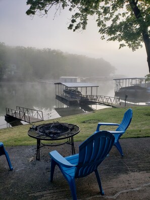 A lakeside view with a fire pit and blue chairs, a dock, and a covered area with boats. - Waterfront Cottage!  Dogs welcome!  Have Fun, Relax and enjoy the lake! MM8 (Gravios Mills)