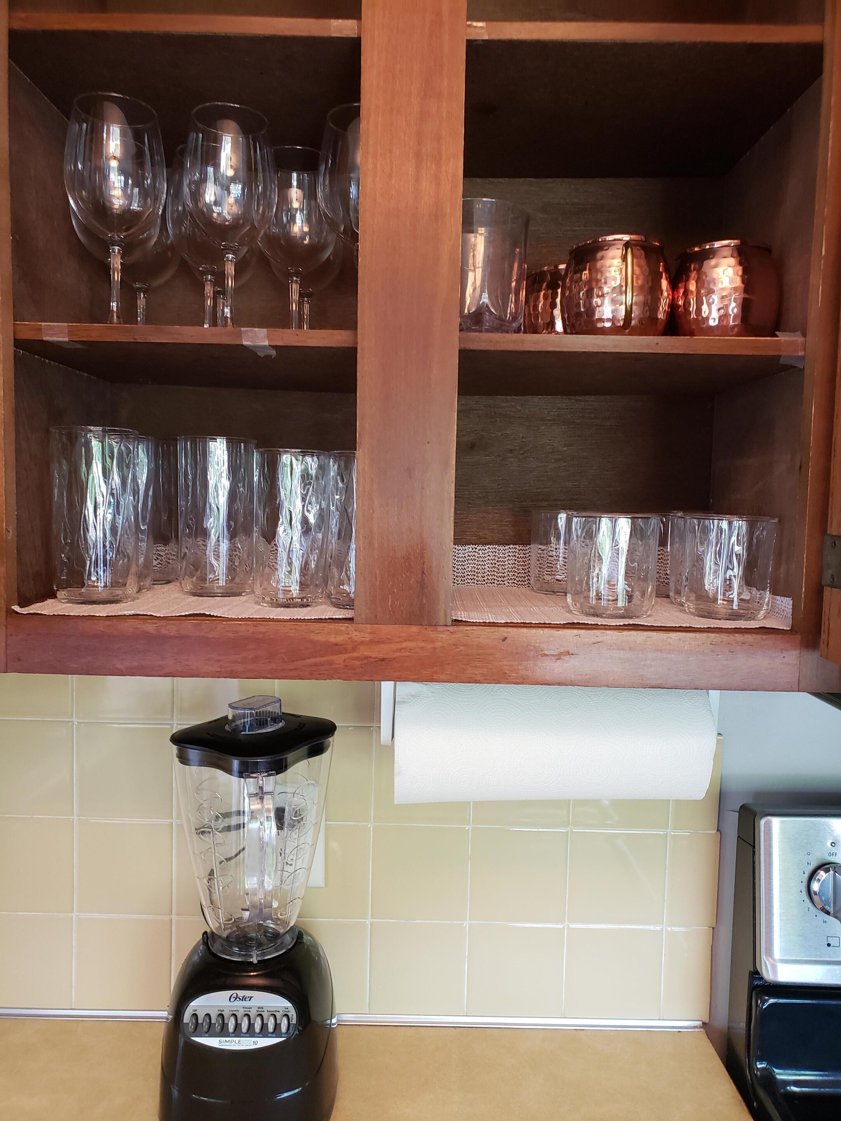 A kitchen with a wooden cabinet containing wine glasses and copper pots. A blender is on the counter.
