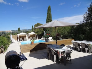 Un área de piscina al aire libre con sillones de descanso, una parrilla y una mesa con sombrillas.