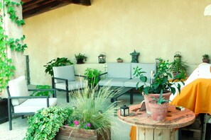An outdoor seating area with chairs and tables, surrounded by potted plants and a wooden bench.