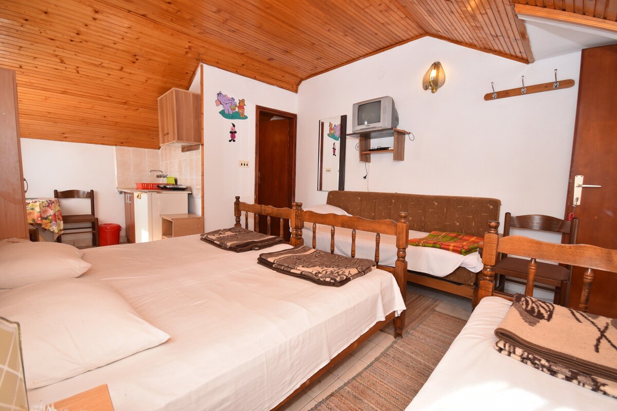 Une pièce chaleureuse avec un plafond en bois, un lit agrémenté de plusieurs oreillers, une petite télévision fixée au mur et une armoire en bois.