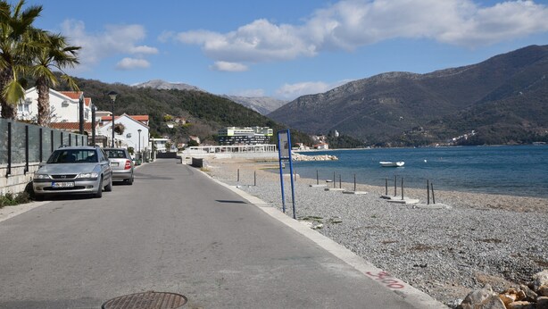 Une route côtière bordée de voitures garées, une plage et des montagnes en arrière-plan.