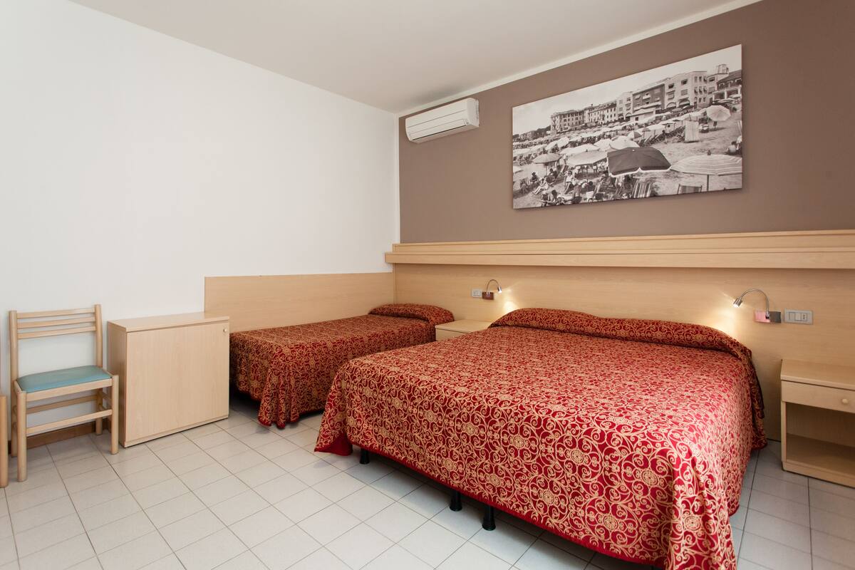 A room with two single beds, a wooden desk, a chair, and a wall-mounted air conditioner.