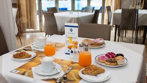 Aamiaispöytä, jossa on croissantteja, leivonnaisia, kahvia ja appelsiinimehua, hotellissa.