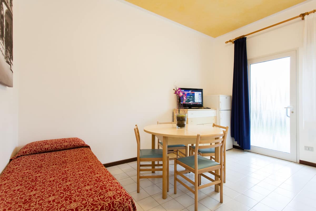 A small room with a bed, a table with chairs, a television, and a window with curtains.