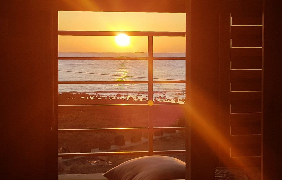 Une chambre avec une fenêtre donnant sur une plage au coucher du soleil.