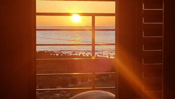 Une chambre avec une fenêtre donnant sur une plage au coucher du soleil.
