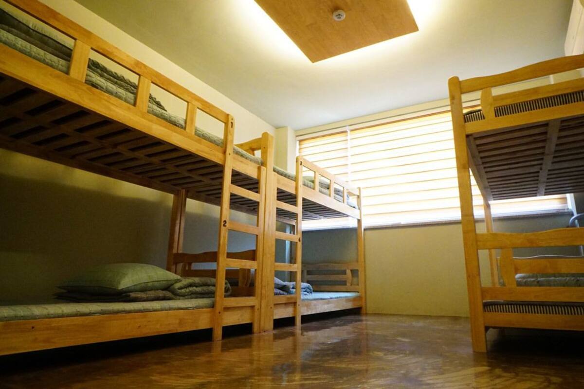 Ein Zimmer mit drei Holzbettstapeln, einem Fenster mit Jalousien und einer Holzdachdecke.