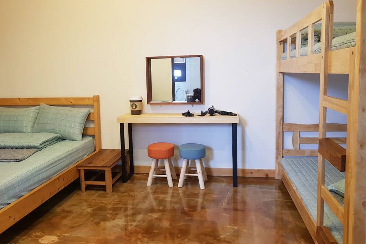 Ein Zimmer mit einem Etagenbett, einem Schreibtisch mit Spiegel, zwei Hocker und einem kleinen Tisch.