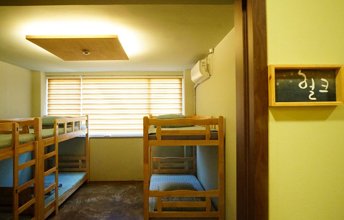 A room with bunk beds, a window with blinds, a ceiling light, and a wall-mounted air conditioner.