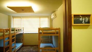 A room with bunk beds, a window with blinds, a ceiling light, and a wall-mounted air conditioner.