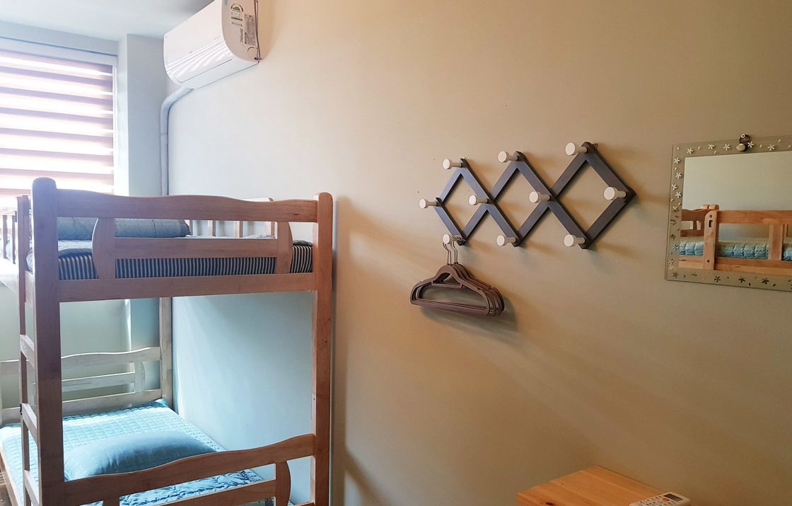 A bunk bed with a wooden frame and a blue mattress, a wall-mounted light fixture, and a mirror with a decorative frame.