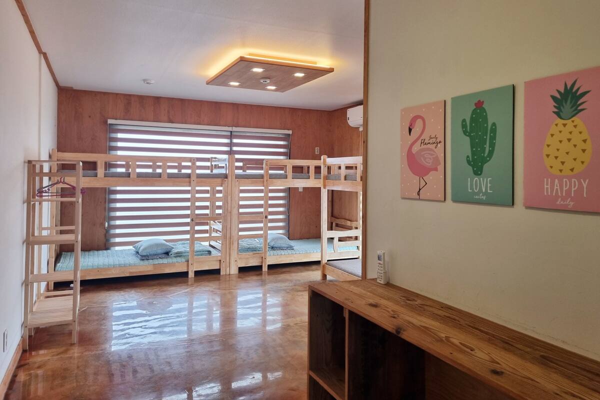 Ein Zimmer mit Etagenbetten, Holzboden, einer Deckenleuchte und Wandbildern.