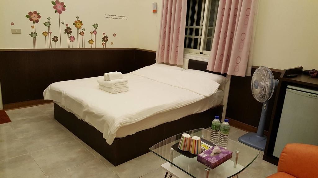 A hotel room with a bed, a glass table with toiletries, a fan, and a window with curtains.
