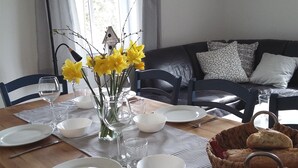 Ruokapöytä on katettu lautasilla, kulhoilla ja maljakossa on keltaisia kukkia. Pöydällä on myös leipäkori.