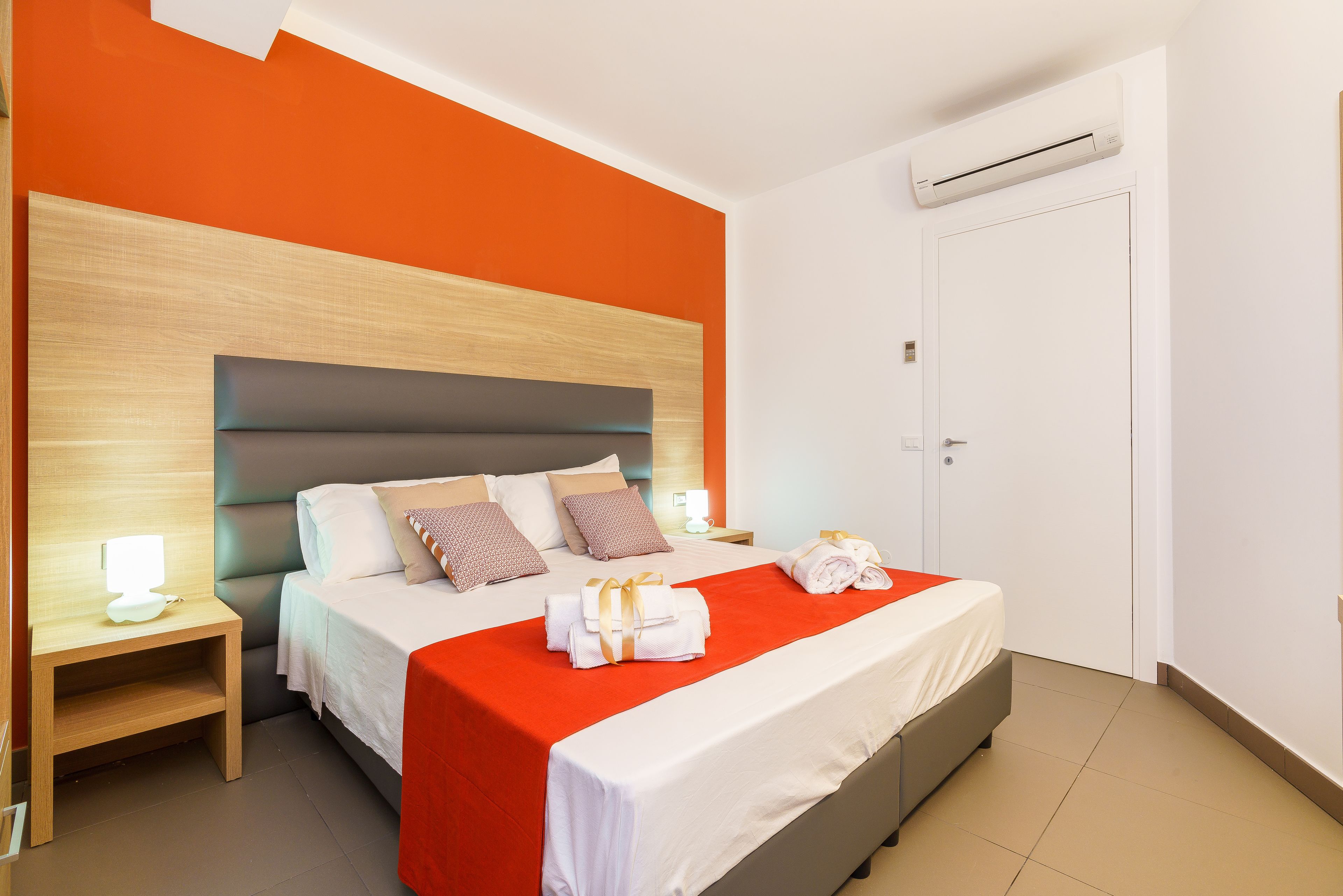 Una habitación de hotel con cama, mesita de noche y aire acondicionado.