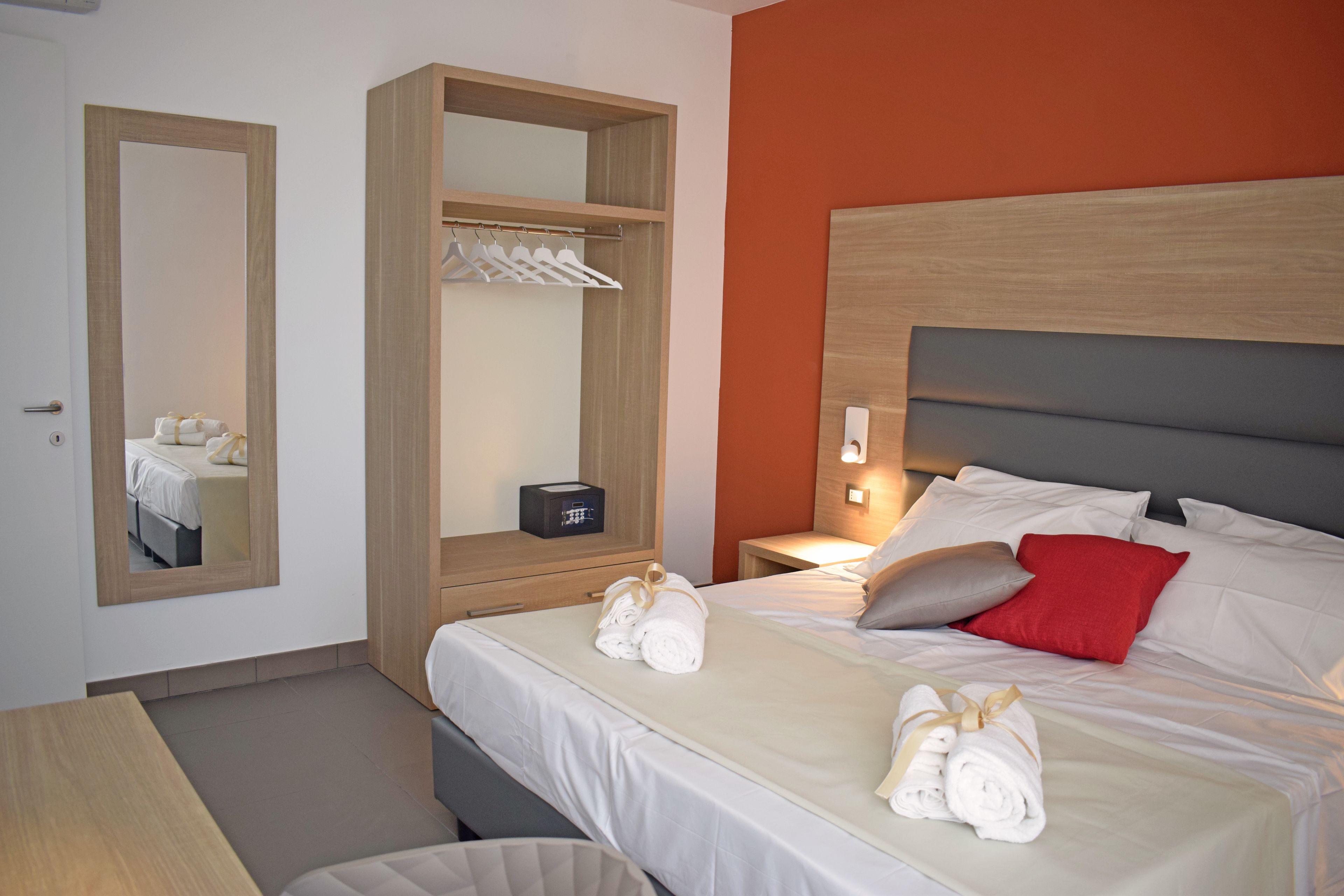 Een hotelkamer met een bed, nachtkastje, kledingkast en een spiegel.