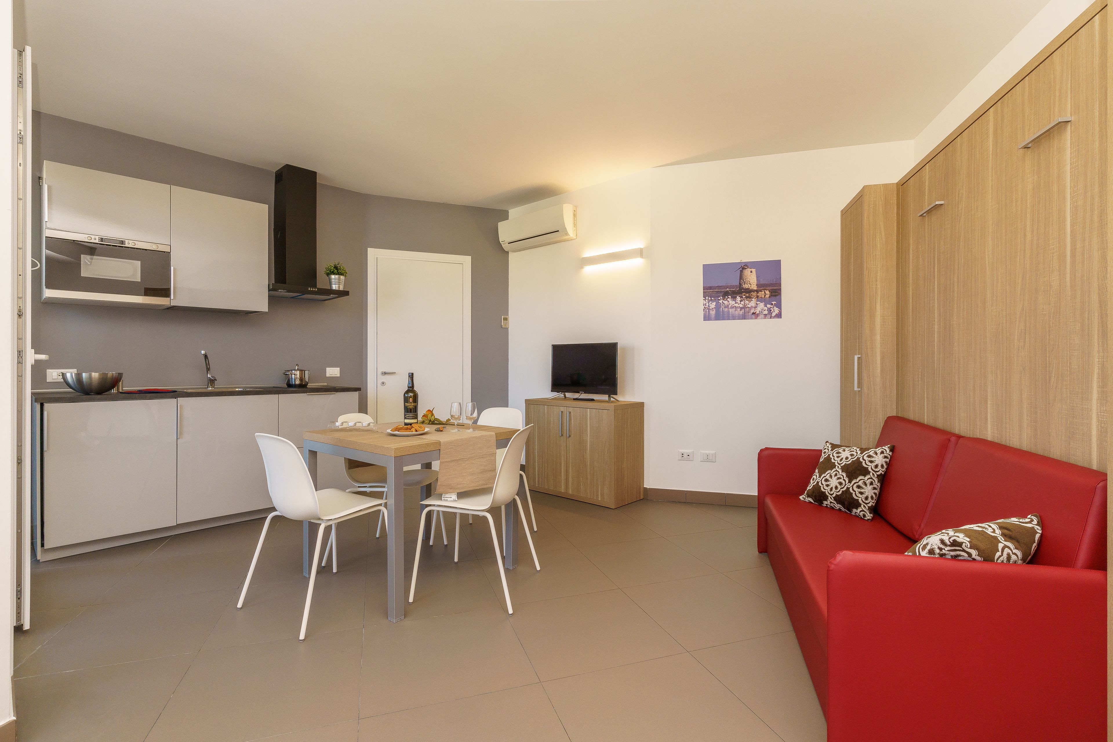 Un espacio habitable pequeño con kitchenette, comedor y un sofá rojo.