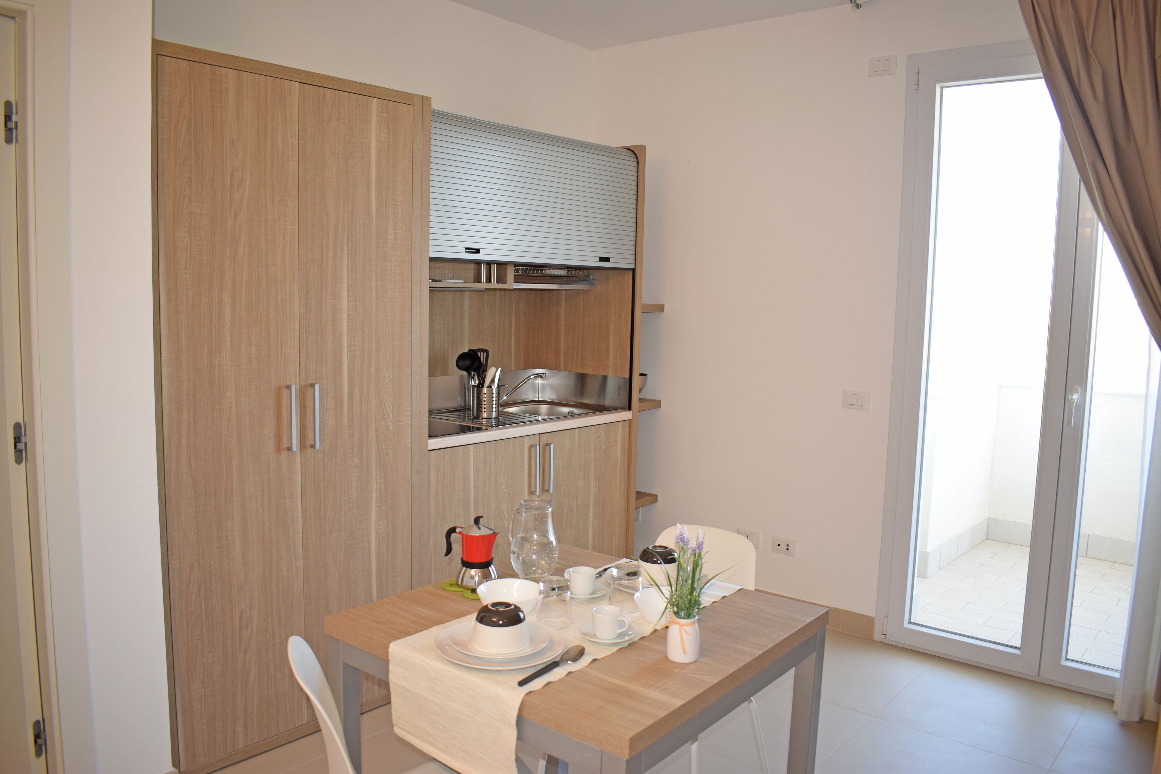A compact kitchen with a built-in oven, a sink, and a window overlooking a balcony.