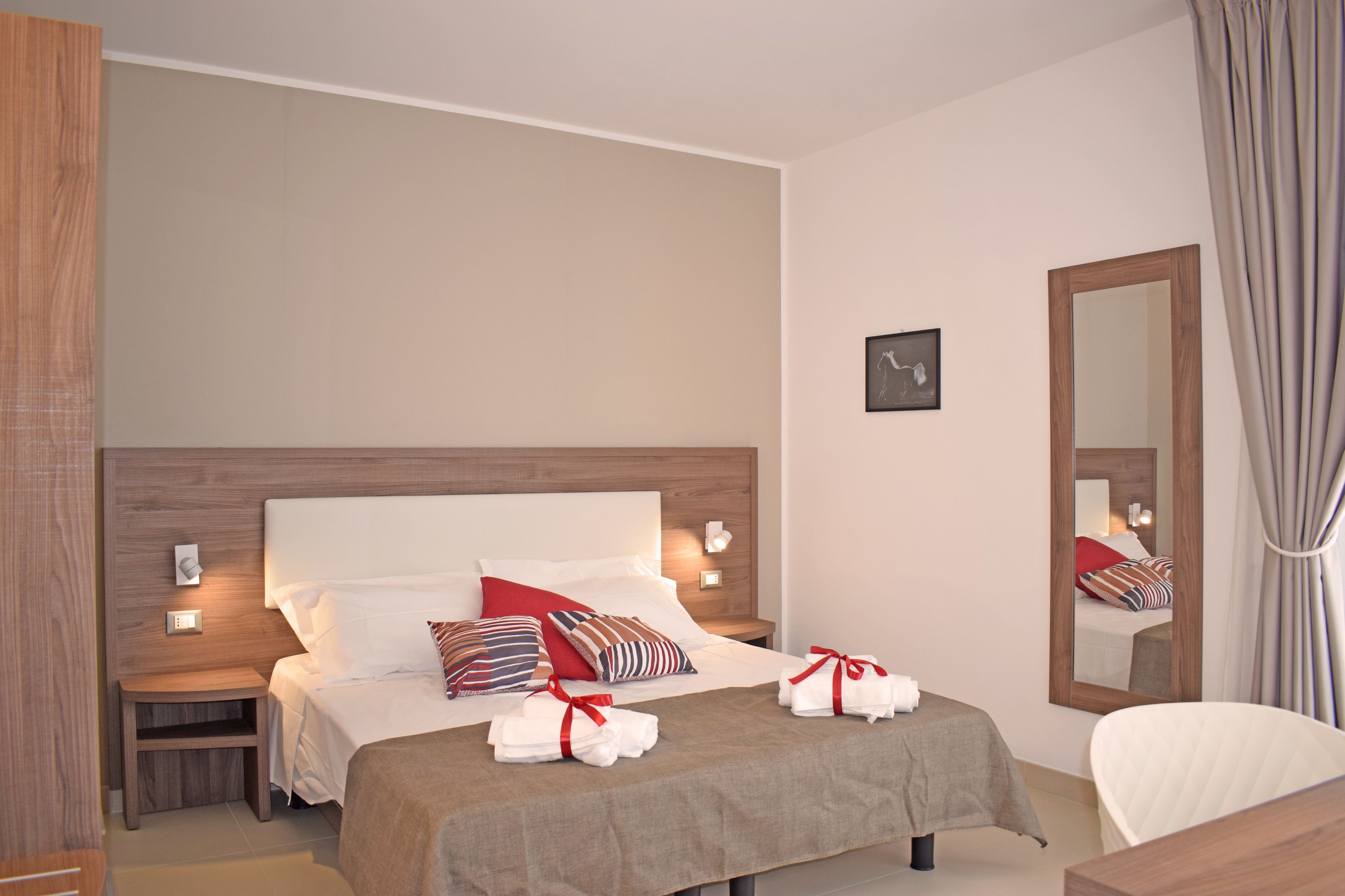 A hotel room with a bed, bedside tables, a mirror, and a chair.