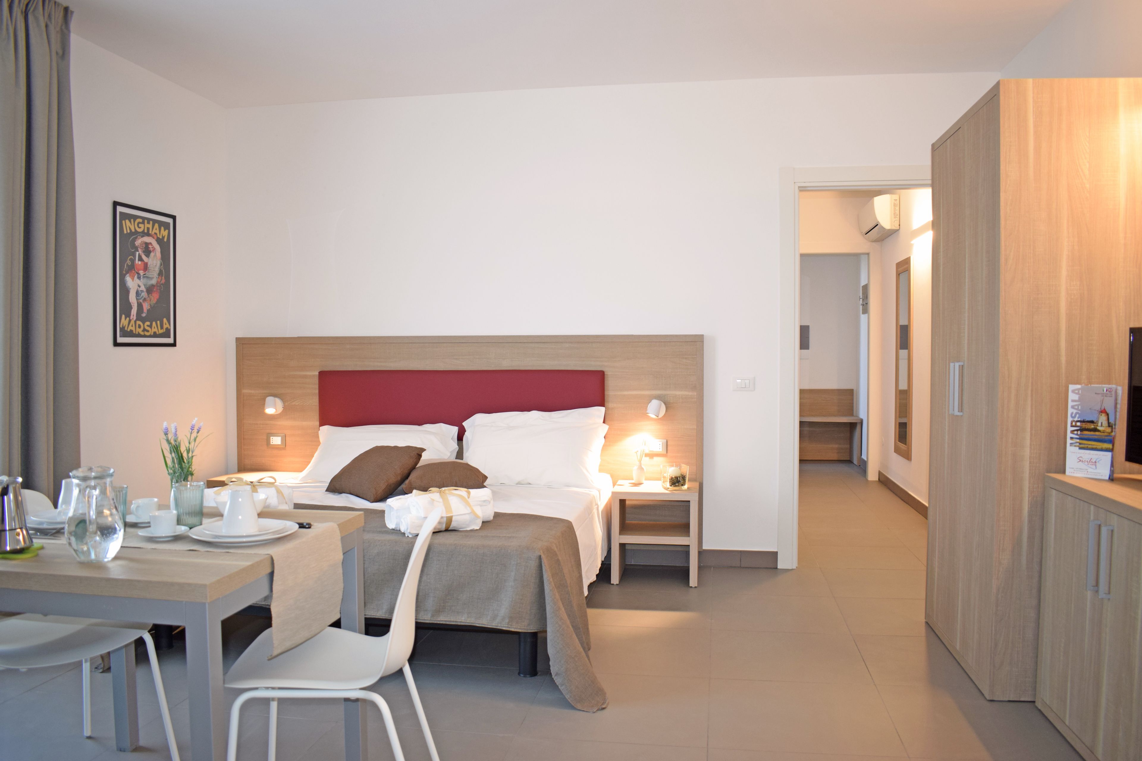 Una habitación de hotel con cama, mesitas de noche, escritorio con sillas y una mesa de comedor.