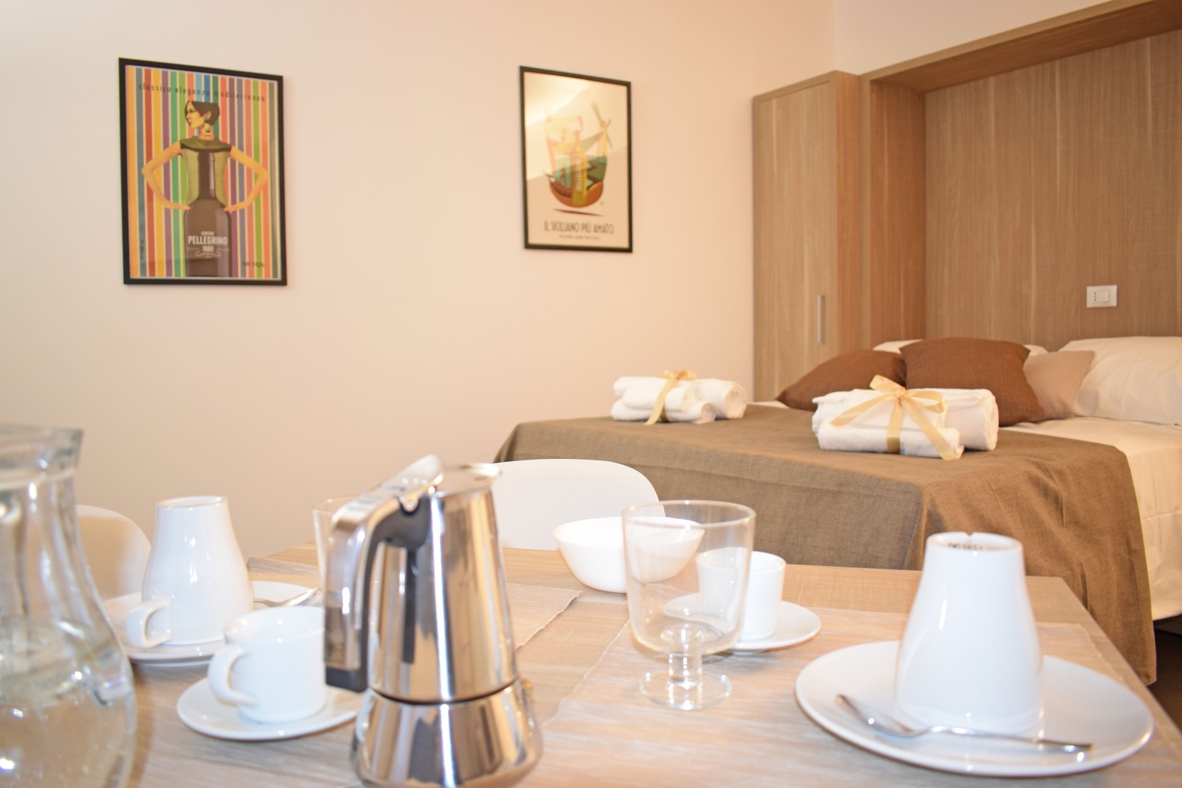 A hotel room with a neatly made bed, a dining table set with white tableware, and two framed artworks on the wall.