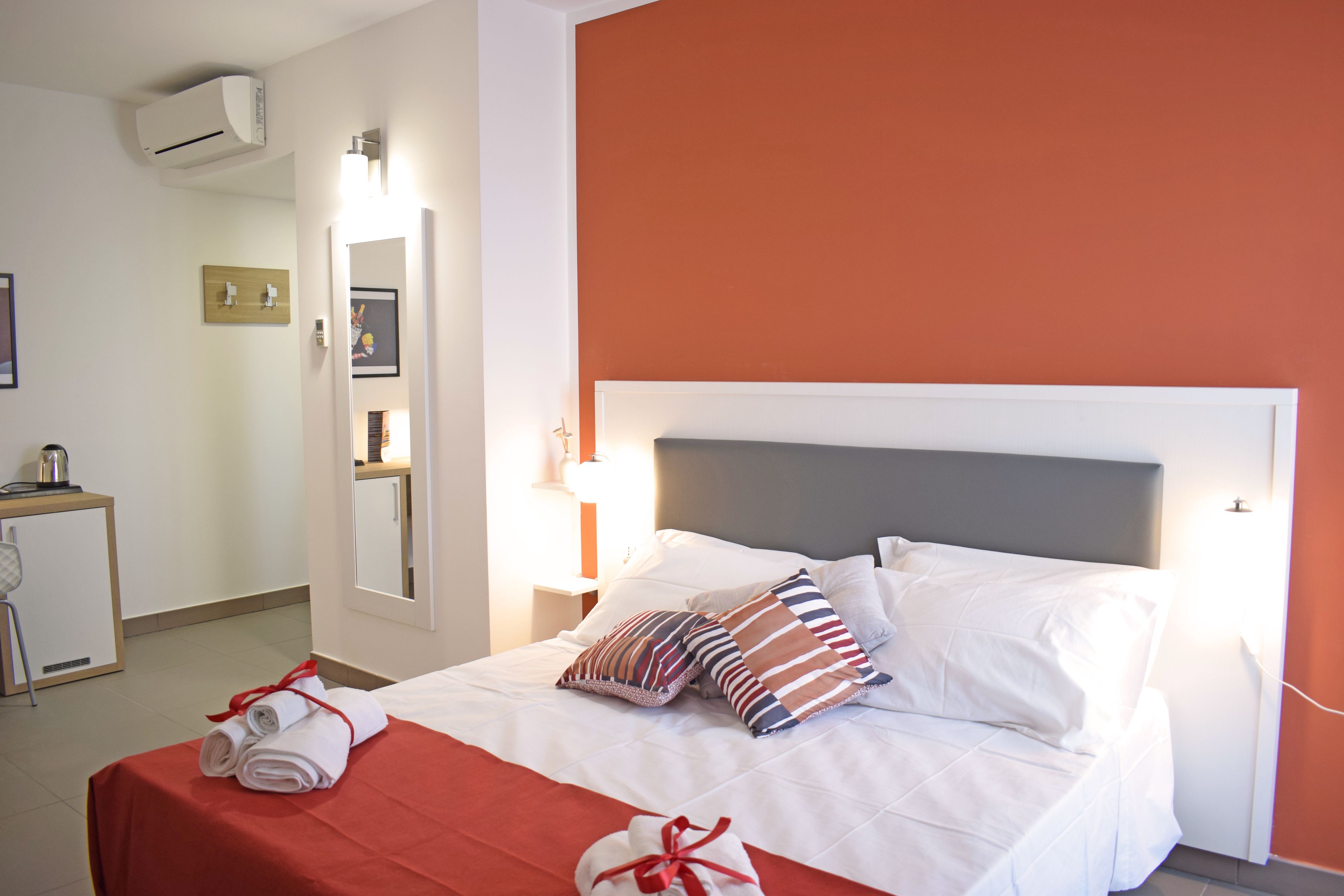 A hotel room with a bed, a bedside table, a mirror, and an air conditioning unit.