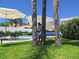 Área da piscina com espreguiçadeiras, guarda-sóis e um homem sentado em uma mesa.