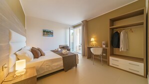 A modern hotel room with a bed, bedside table, desk, chair, and wardrobe. - Travini Hotel Residence (Marsala)