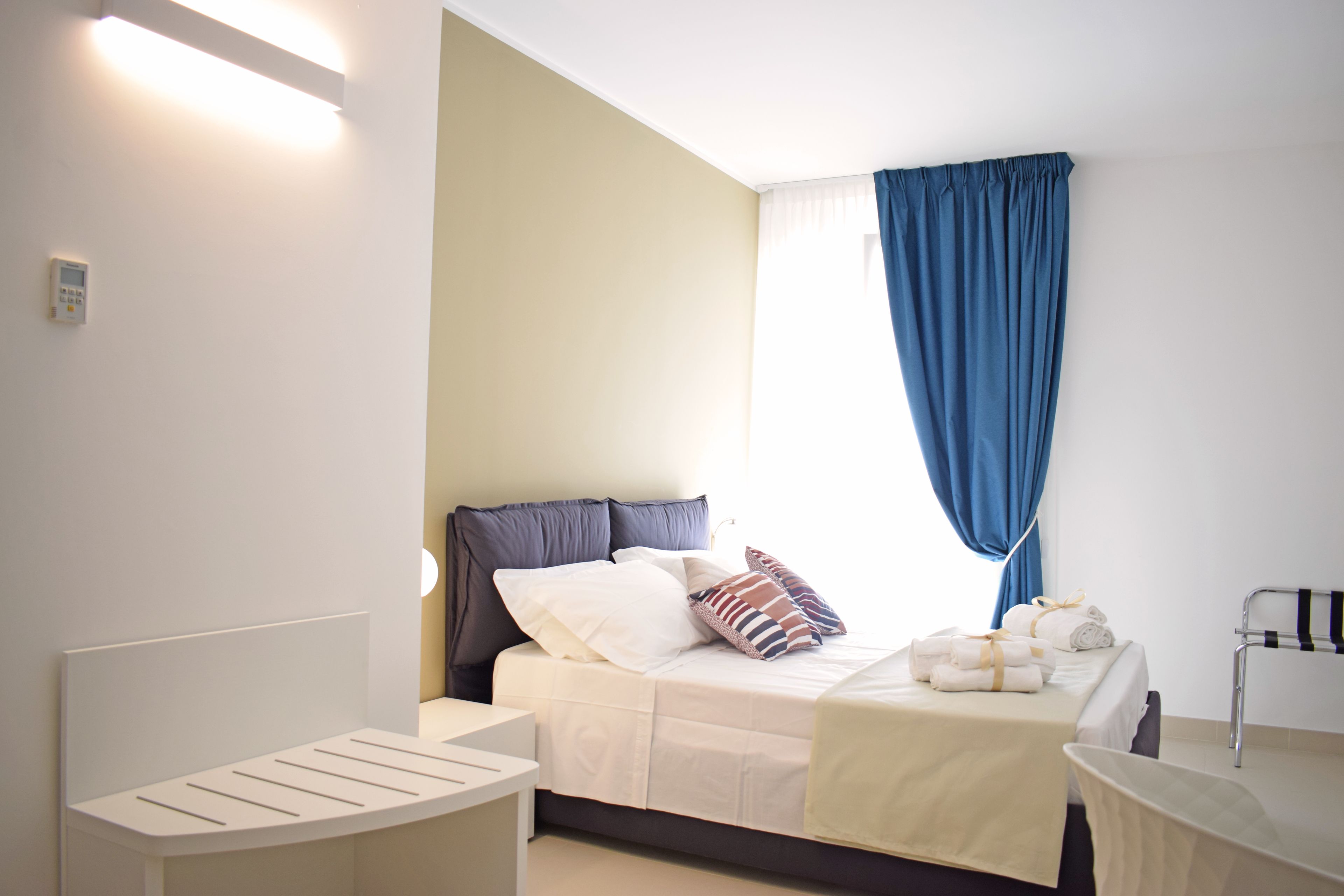A hotel room with a bed, bedside table, and a window with curtains.