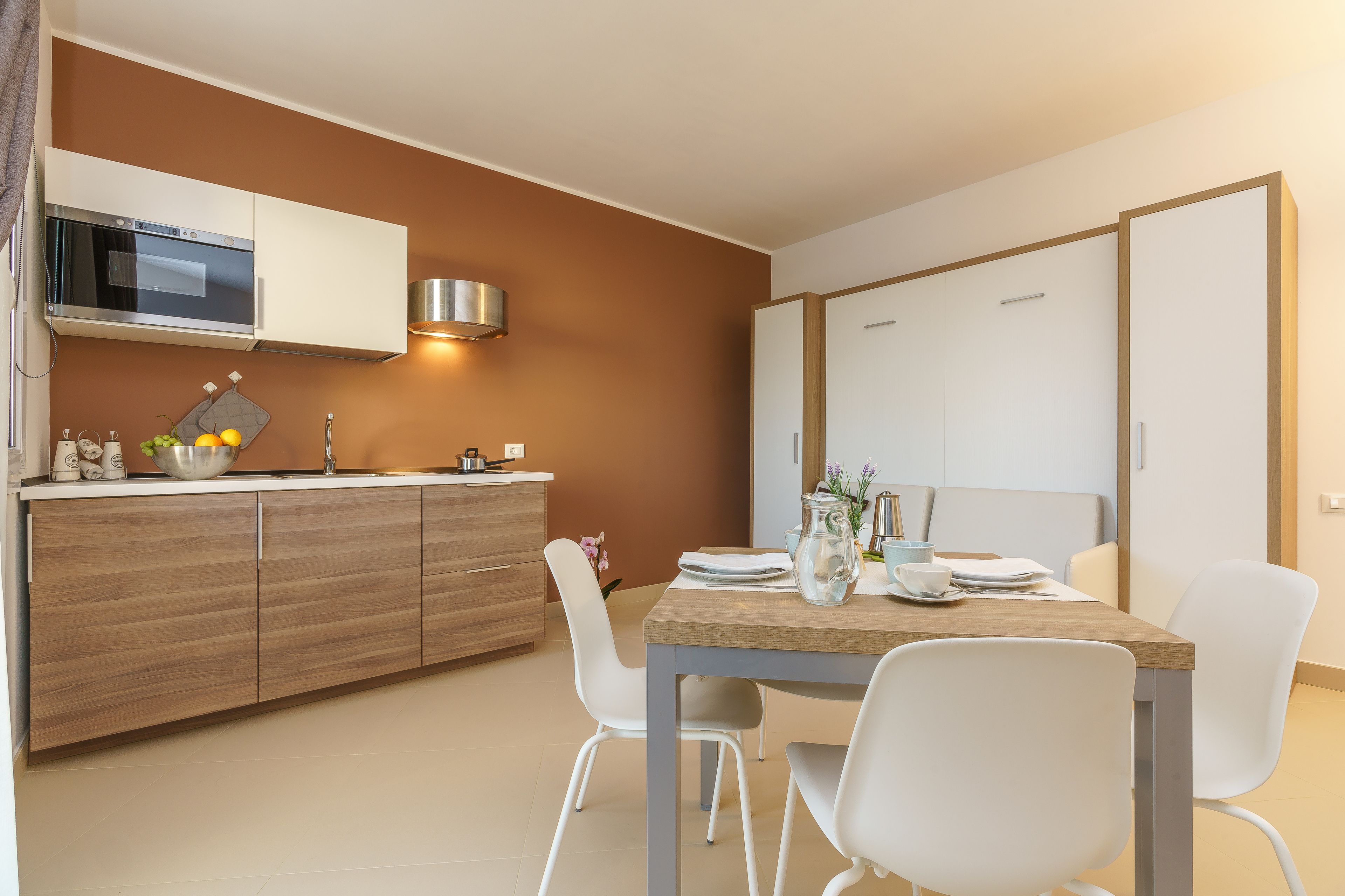 Une cuisine moderne équipée d’un four à micro-ondes, d’un four et d’un évier. On y trouve une table à manger avec des chaises et un vase rempli de fleurs.